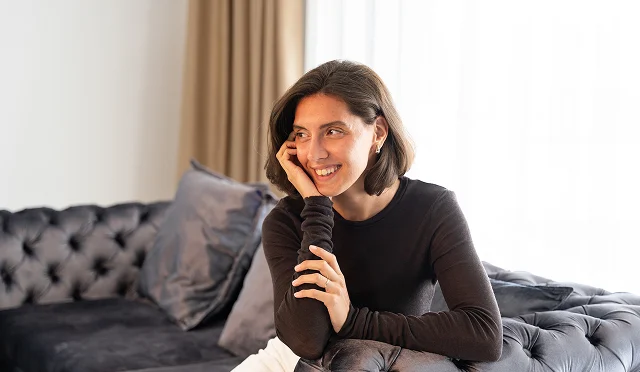 Anastasia sitzt entspannt auf dem Sofa und lächelt in einem hellen Raum