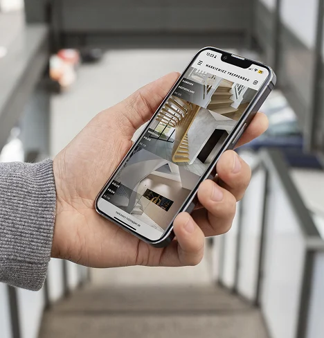 Hand hält ein Smartphone mit der geöffneten Website einer Tischlerei, die hochwertige Treppenlösungen zeigt.