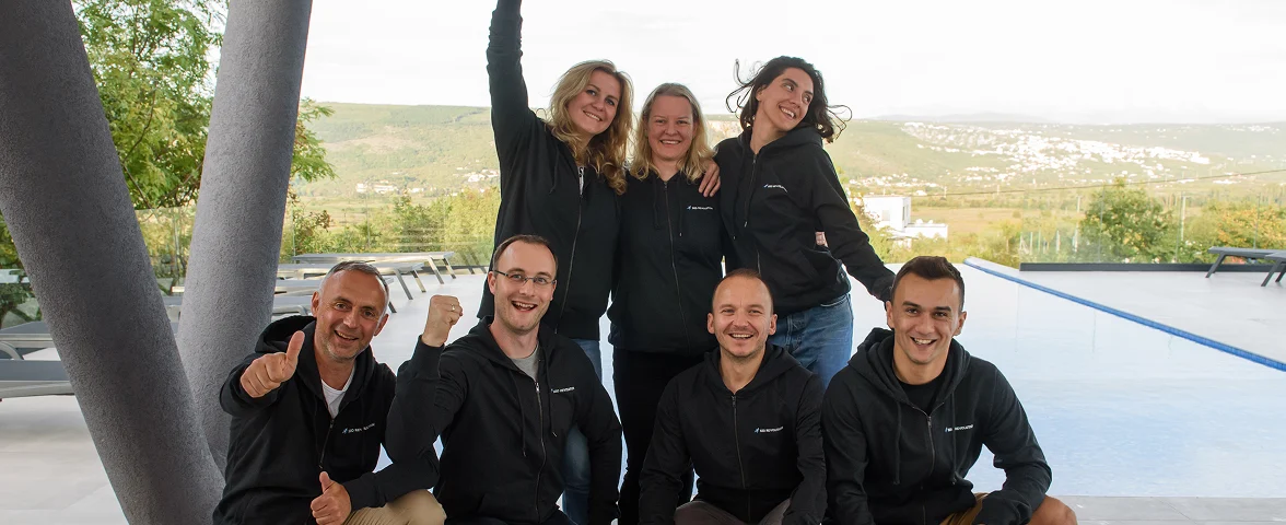 Team von SEO Revolution posiert lachend in Freizeitkleidung vor einem Pool mit Aussicht auf die Berge