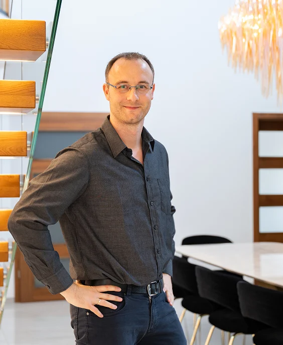 Mann steht lächelnd neben einer Treppe und blickt selbstbewusst in die Kamera