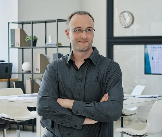Porträtfoto von Toni Frisch in einem modernen Büro, mit verschränkten Armen und freundlichem Blick zur Seite