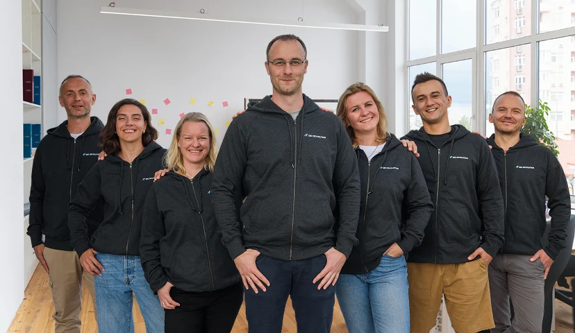 Gruppenfoto des SEO Revolution Teams in einem hellen Büro, alle tragen dunkle Hoodies mit dem Agenturlogo.